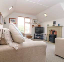 A living room with beige sofas a television on a stand a fireplace and framed pictures on the wall at The Watch in Porthcurno