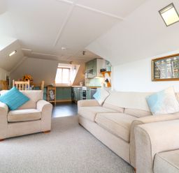 An open plan living room and kitchen with beige sofas and wooden dining table at The Watch in Porthcurno