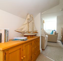 A wooden cabinet with a model sailboat and books next to a seating area and dining table at The Watch in Porthcurno