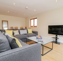 A living room with grey sofas yellow patterned cushions a coffee table with board games and a flat-screen TV on a stand at Oak Lodge in Sheriff Hutton