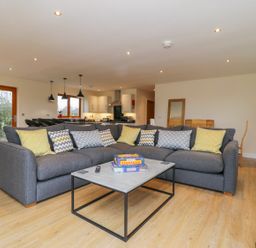 A living room with a gray sectional sofa and patterned cushions a coffee table and a kitchen in the background at Oak Lodge in Sheriff Hutton