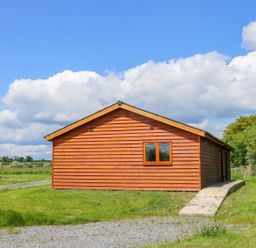 A wooden cabin with a single window and a concrete pathway surrounded by grass at Oak Lodge in Sheriff Hutton