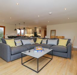 A living room with a grey sectional sofa with patterned cushions a coffee table and an open kitchen at Rose Lodge in Sheriff Hutton
