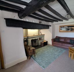 A living room with a brown leather sofa a green rug a wooden side table and a black fireplace at Gwrtheyrn in Dyffryn Ardudwy