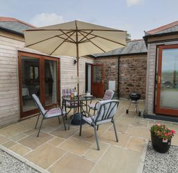 An outdoor patio area with a table and four cushioned chairs under a large umbrella outside a building at Edwin's View in Nancegollan nr Porthleven