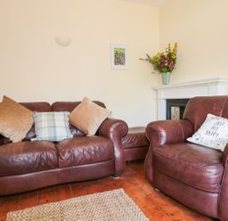 A living room with brown leather sofas with cushions wooden floor a rug and a fireplace with flowers at School House in Builth Wells