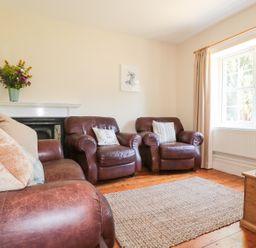 A living room with leather armchairs wooden floor a rug a window with curtains and a wooden chest at School House in Builth Wells