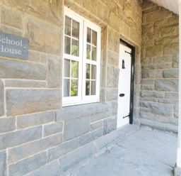 Stone exterior wall with a white window and a white door beside a sign reading School House at School House in Builth Wells