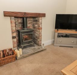 A room with a wood burning stove and a television on a stand at Hare & Hounds House in Allendale