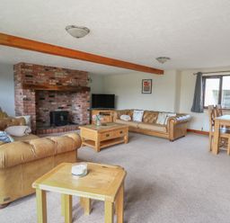 A living room with a fireplace and a dining table at Glanyrafon in St Harmon