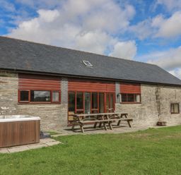 An outdoor patio area with a hot tub and seating at Glanyrafon St Harmon