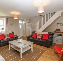 A living room with two leather sofas with red cushions a wooden coffee table a red armchair and stairs at Glasfryn in Llanfaethlu