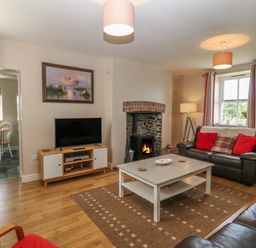 A living room with leather sofas a coffee table a television and a wood-burning stove at Glasfryn in Llanfaethlu