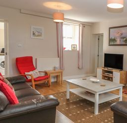 A living room with brown leather sofas a red armchair a white coffee table a television and a fireplace at Glasfryn in Llanfaethlu