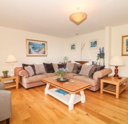 A living room with a beige sofa and wooden coffee table with flowers at Wood View Cottage in Blackawton