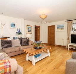A living room with a sofa, armchair, wooden coffee table, TV on a stand, paintings on the walls and wooden doors at Wood View Cottage in Blackawton