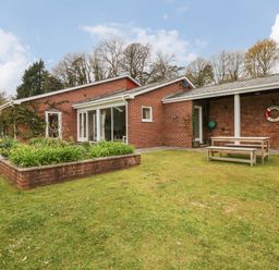 A brick house with a garden bed and a wooden picnic table on grass at Wood View Cottage in Blackawton