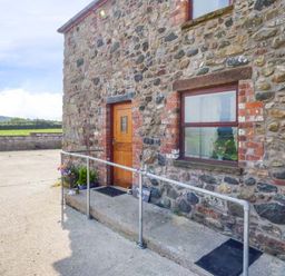 Stone exterior wall with a wooden door and window with metal railing on concrete steps at Muncaster View in Carleton near Ravenglass