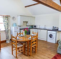 A kitchen and dining area with wooden table and chairs washing machine and green armchair at Muncaster View in Carleton near Ravenglass