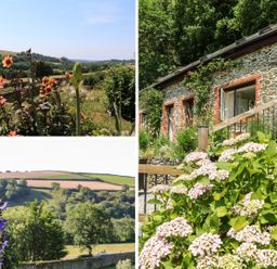 A garden with flowers and greenery outside a stone cottage with wooden railing at Rose Cottage in Barnstaple
