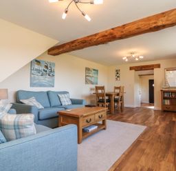 A living room with blue sofas wooden tables a dining table paintings and a bookshelf at Rose Cottage in Barnstaple