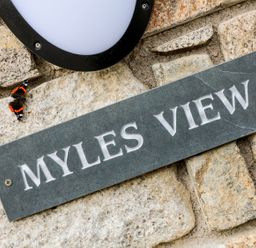 A stone wall with a black plaque that reads Myles View and a butterfly near a black and white wall light at Myles View in Pendeen