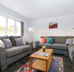 A living room with grey sofas and a wooden coffee table on a colorful rug at Myles View in Pendeen