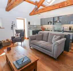 A living room with a sofa and kitchen area at Apple Tree Cottage near Bleatarn near Kirkby Stephen