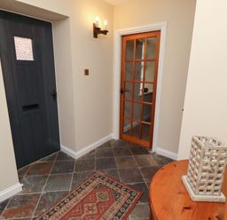 An entryway with a dark wooden front door a glass-paneled wooden interior door a small rug on tiled floor and a wooden table with a decorative lantern Bracken Lodge Wooler