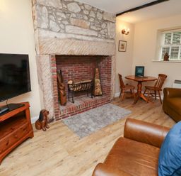 A living room with a stone and brick fireplace two brown leather armchairs a wooden round table with two chairs and a television on a wooden stand at Bracken Lodge in Wooler