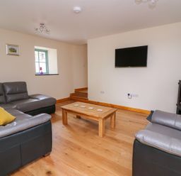 A living room with grey leather sofas a wooden coffee table a wall-mounted television and a wood-burning stove at Bwthyn Eisteddfa Fach in Brynberian near Newport