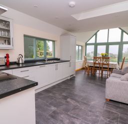 A kitchen and dining area with large windows and a gray sofa at Bwthyn Eisteddfa Fach in Brynberian near Newport