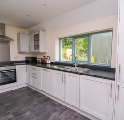 A kitchen with white cabinets a black countertop a stainless steel oven and hood a sink under a window at Bwthyn Eisteddfa Fach in Brynberian near Newport