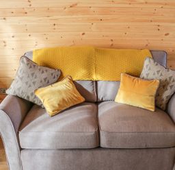 A gray sofa with four cushions and a yellow throw against a wooden wall at Dingle Den in Craswall