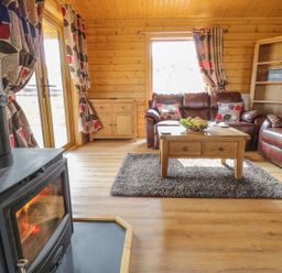 A living room with a wood burning stove sofas coffee table and wooden shelves at Manor Farm Lodges - Red Kite Lodge in Newtown