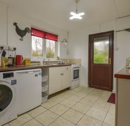 A kitchen with a washing machine microwave stove and red window blind at The Quillet in Pendeen