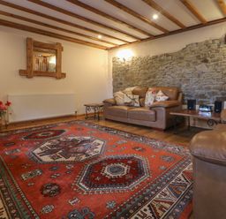 A living room with leather sofas a red patterned rug and a stone wall at Post House in Holsworthy