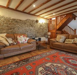 A living room with two leather sofas a wooden coffee table and a red patterned rug at Post House in Holsworthy