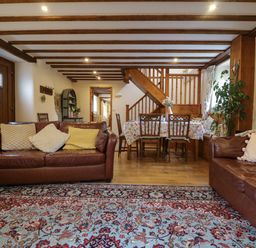A living room with two brown leather sofas a dining table with chairs and floral tablecloth wooden beams on ceiling and a patterned rug on floor at The Croft in Holsworthy