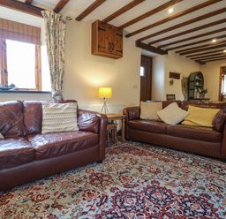 A living room with two brown leather sofas a patterned rug exposed wooden beams and a lamp at The Croft in Holsworthy