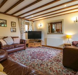 A living room with leather sofas a patterned rug a television on a wooden stand and a large mirror on the wall at The Croft in Holsworthy