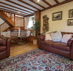 A living room with brown leather sofas a floral rug a wooden dining table with chairs and wooden stairs at The Croft in Holsworthy