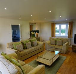 A living room with three sofas a glass coffee table a television and a window at Holly Edge in Moorsholm