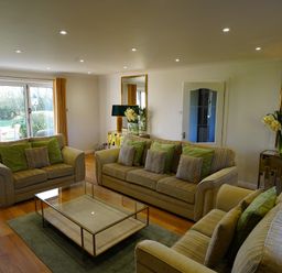 A living room with three sofas a glass coffee table wooden floor and a large window with yellow curtains at Holly Edge in Moorsholm