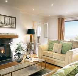A living room with sofas pillows a fireplace a glass coffee table and a large window at Holly Edge in Moorsholm