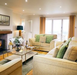 A living room with beige sofas green cushions a glass coffee table with flowers a fireplace and yellow curtains at Holly Edge in Moorsholm