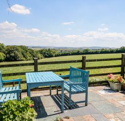 A patio with a blue table and benches overlooking a green field with trees at Janes Place in Lifton