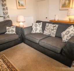 A living room with two dark sofas with patterned cushions two lamps and framed pictures on walls at Janes Place in Lifton