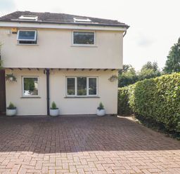A driveway with potted plants in front of a two-story house bordered by a hedge at Palm Court Burton-in-Kendal