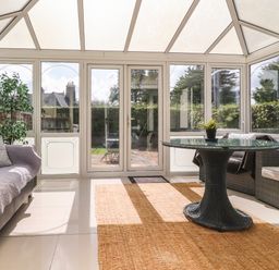 A conservatory with a glass table and wicker chairs and sofas with cushions at Palm Court in Burton-in-Kendal